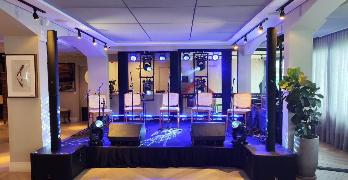 Palco com torres de som, moving beams e iluminação azul montados em um salão